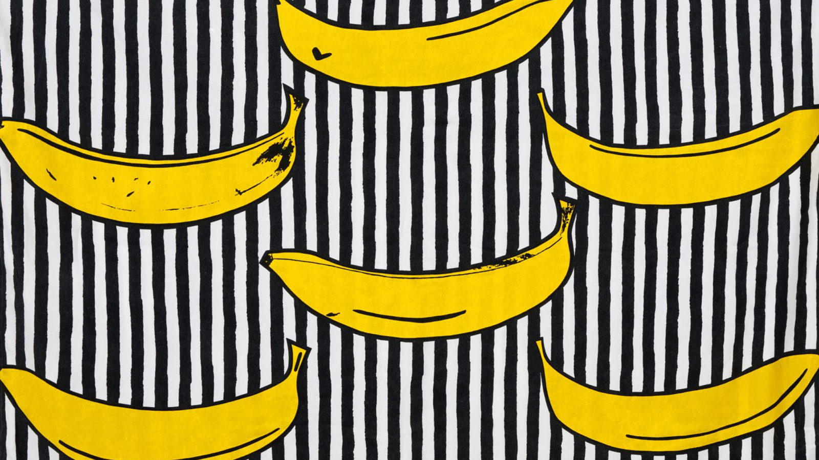The fabric RANDIG BANAN with a bold, naïve yellow banana pattern on a striped white and black background.