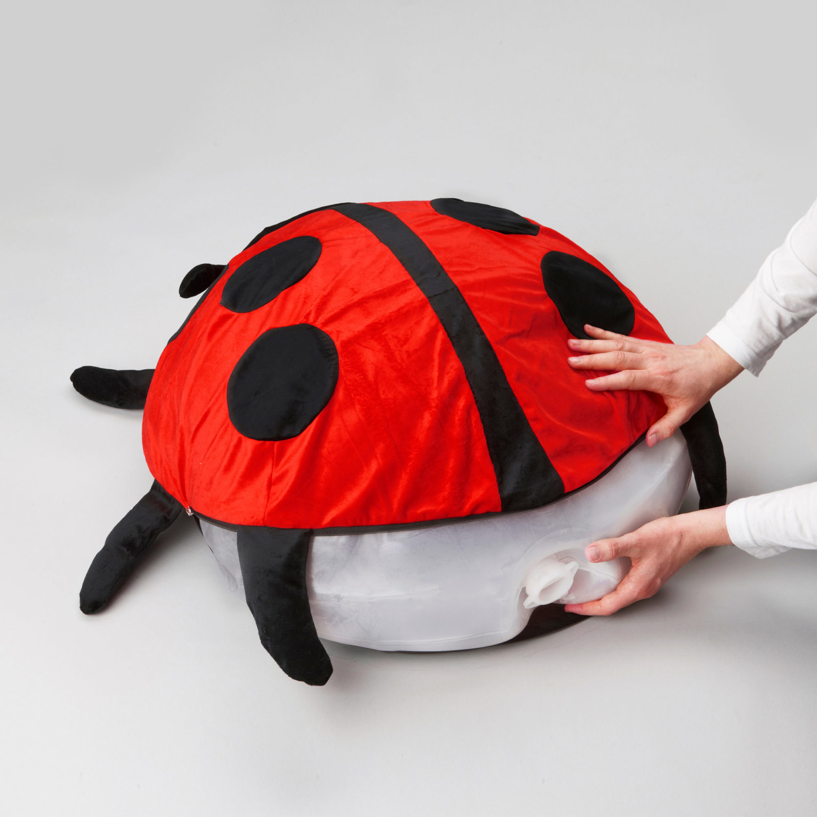 Gros plan sur des mains enfilant une housse coccinelle sur un coussin en plastique gonflé.