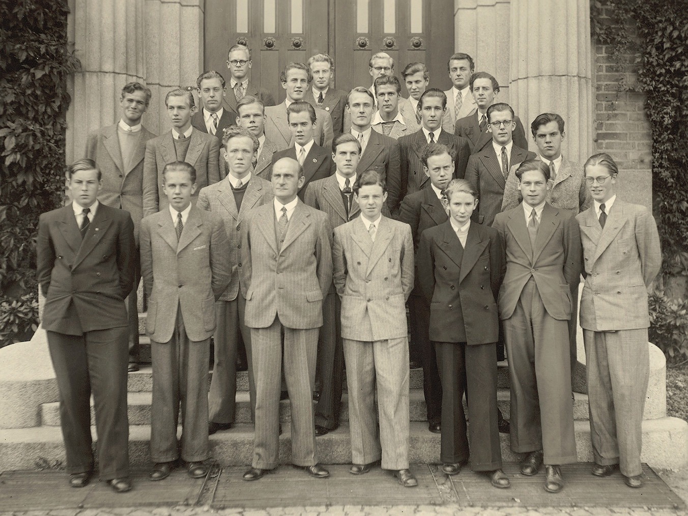 Gruppenfoto, 1940er-Jahre, junge Männer in hellen Anzügen in fünf Reihen vor imposantem Gebäude. Ingvar Kamprad in der Mitte.