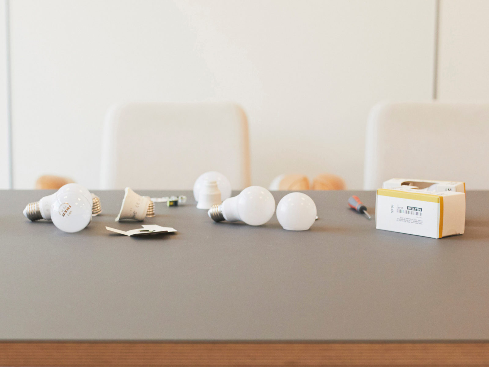 グレーのテーブルの上に散らばるスクリュードライバーと、一部分解されたLED電球のクローズアップ。