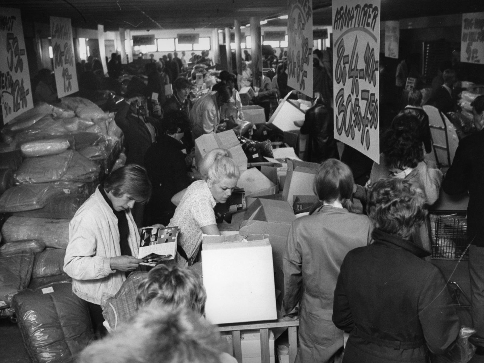 People rummaging through wares and boxes in crowded IKEA store displaying big sale signs.