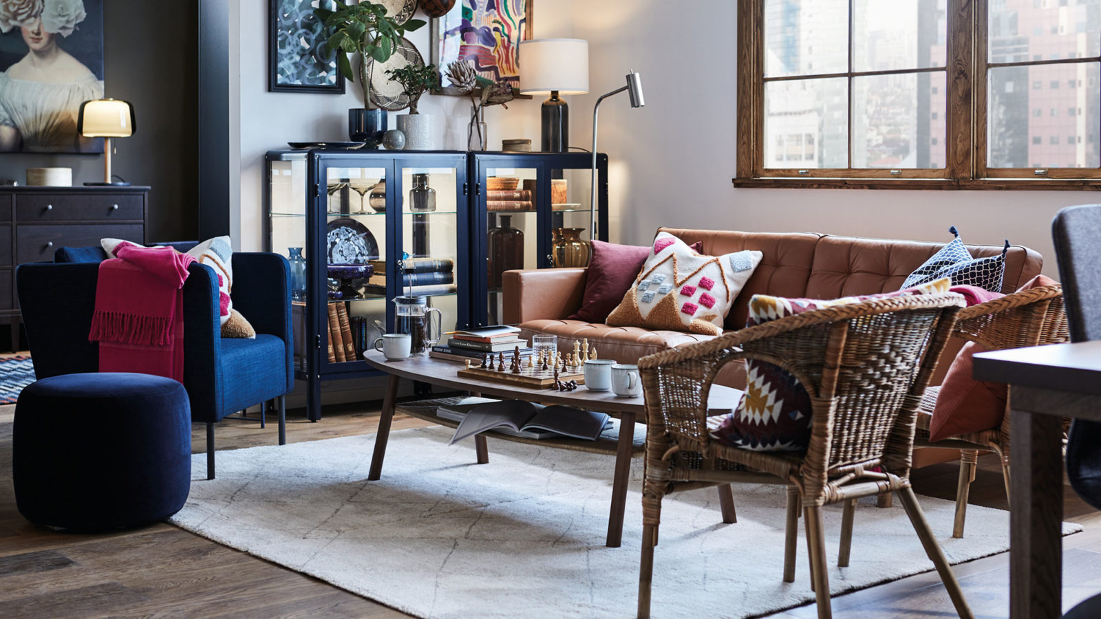 Living room with leather sofa, rattan chairs, blue armchair, grey rug, glass cabinets with books and decorative objects.