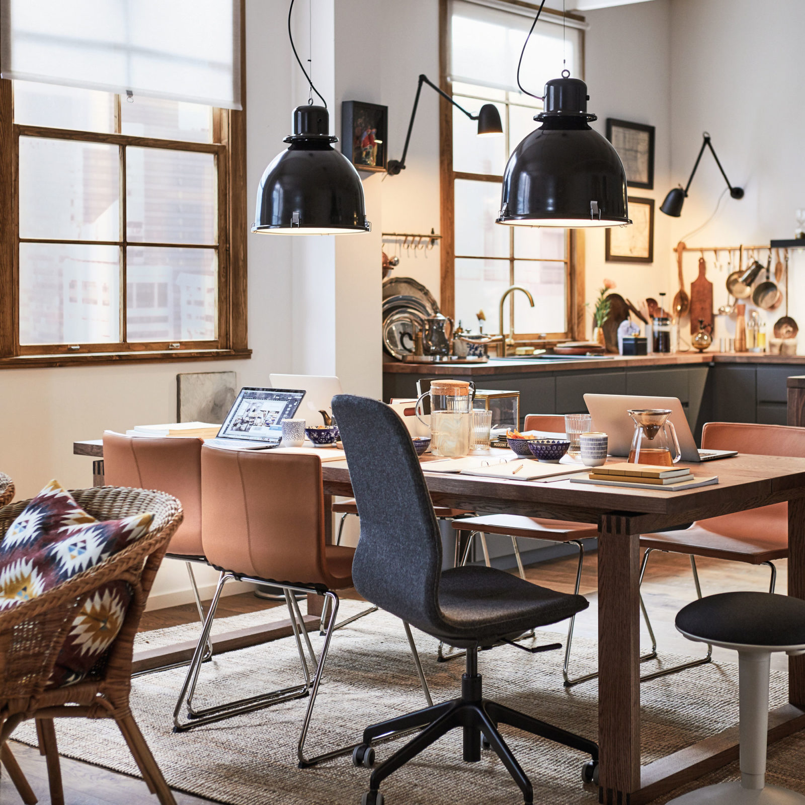 Open plan kitchen and dining area with wooden table on which sit laptops and books, a tea pot, cups and bowls.