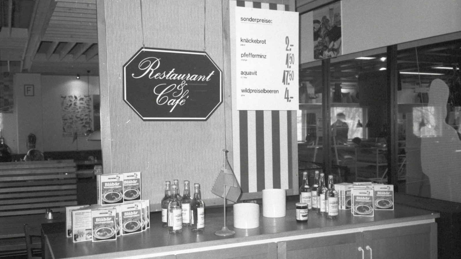 Restaurant with sideboard displaying blueberry soup mix cartons, akvavit bottles and small Swedish desk flag.