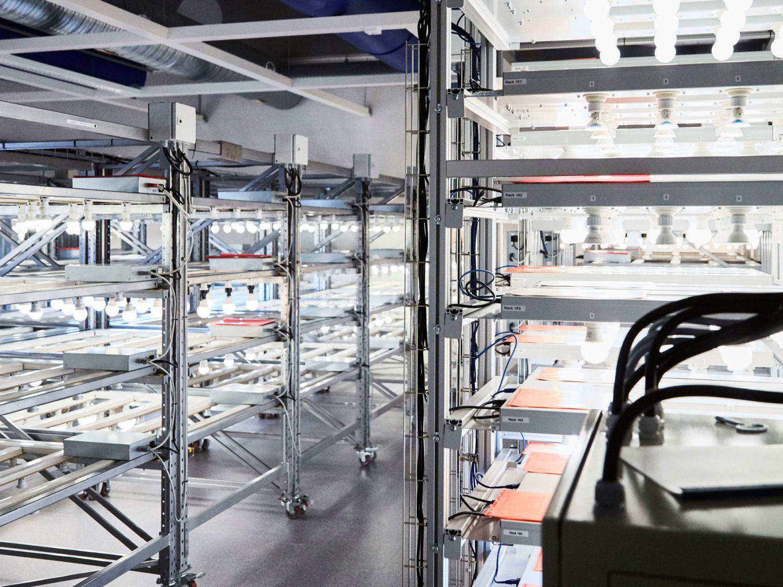 Environnement de laboratoire d’aspect stérile, nombreuses lampes LED allumées sur étagères en aluminium.