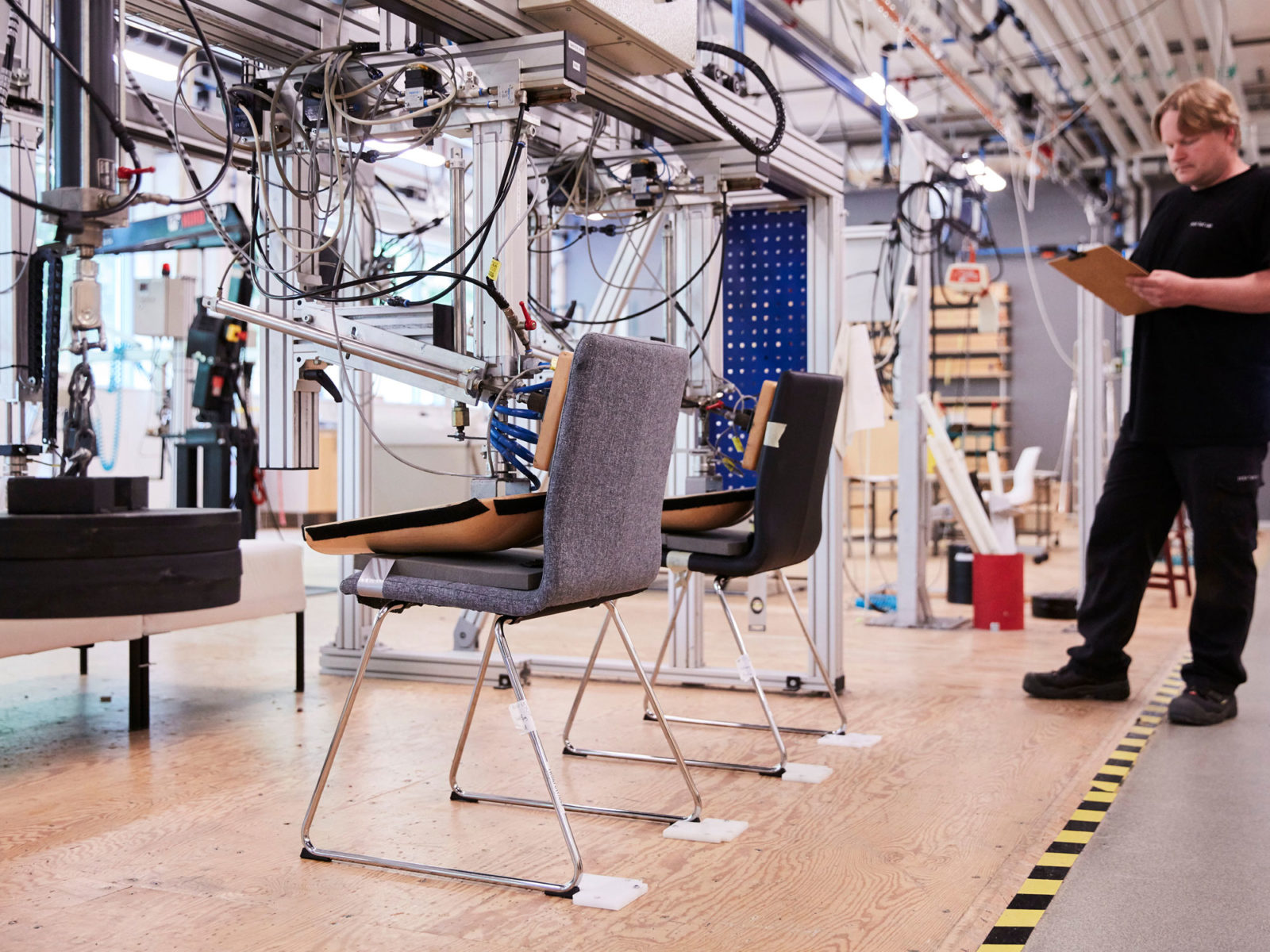 Machines d’essai sophistiquées testant deux chaises dans un environnement moderne. Un homme debout à côté prend des notes.