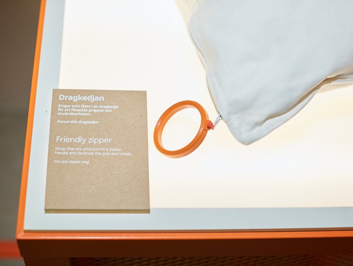 Hörnet av en kudde med en stor, orange plastring fäst vid kuddfodralets blixtlås och en förklarande text bredvid den.