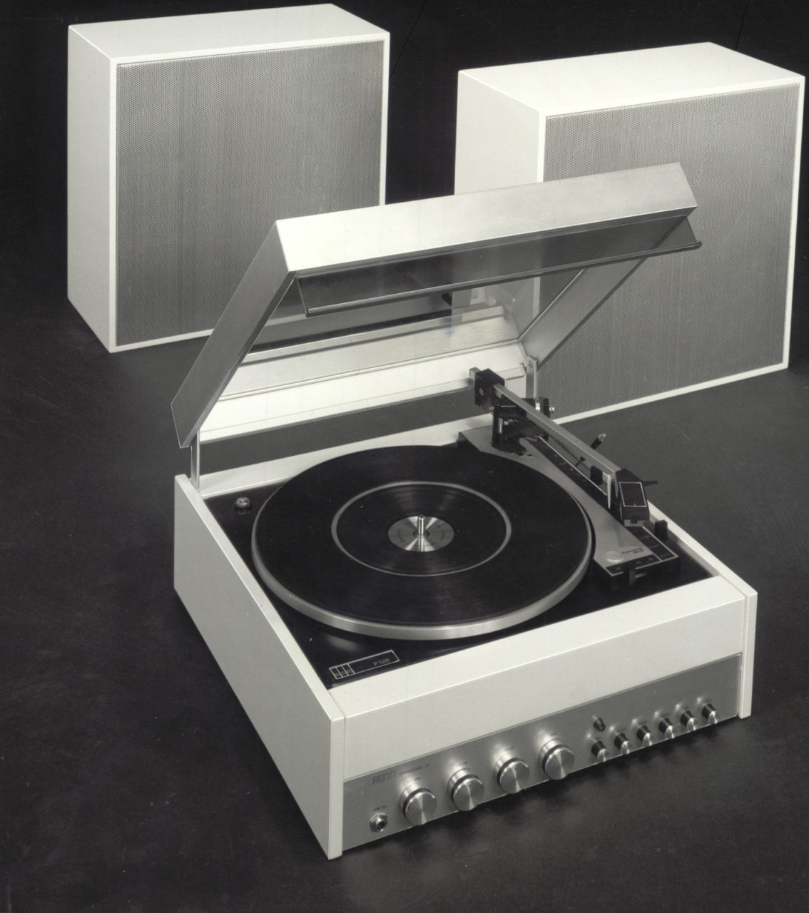 A white and black RENN record player from the 1970s with a transparent, open lid and two white speakers in the background.