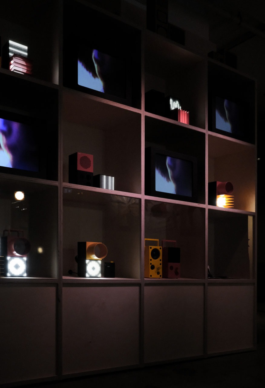 A dark red shelf unit exhibiting the different items of the IKEA FREKVENS portable music collection.