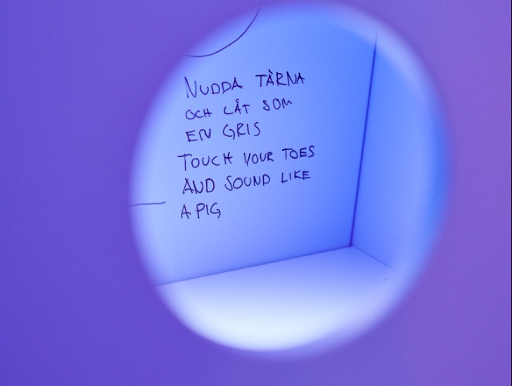 Den handskrivna texten ”touch your toes and sound like a pig” sedd genom ett violett hål.