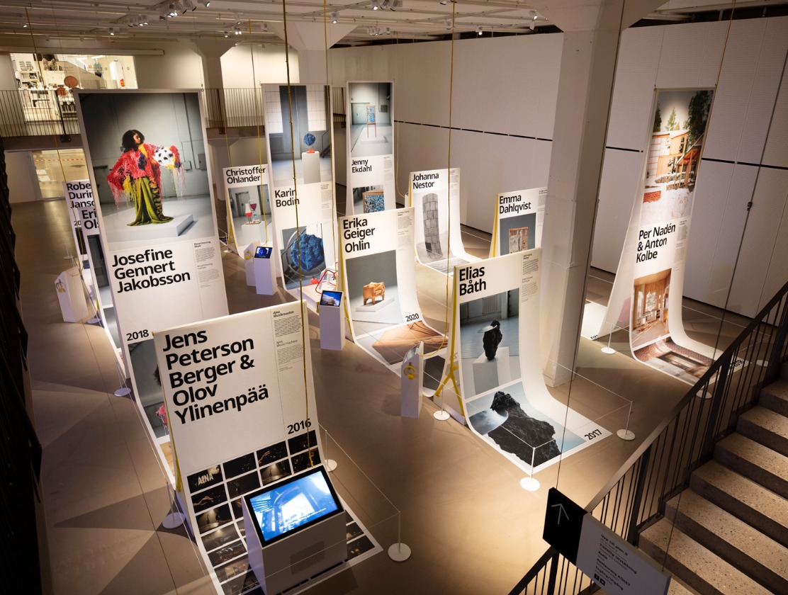 A large room with spotlights and exhibition posters printed on long sheets of paper arranged to create wavelike shapes.