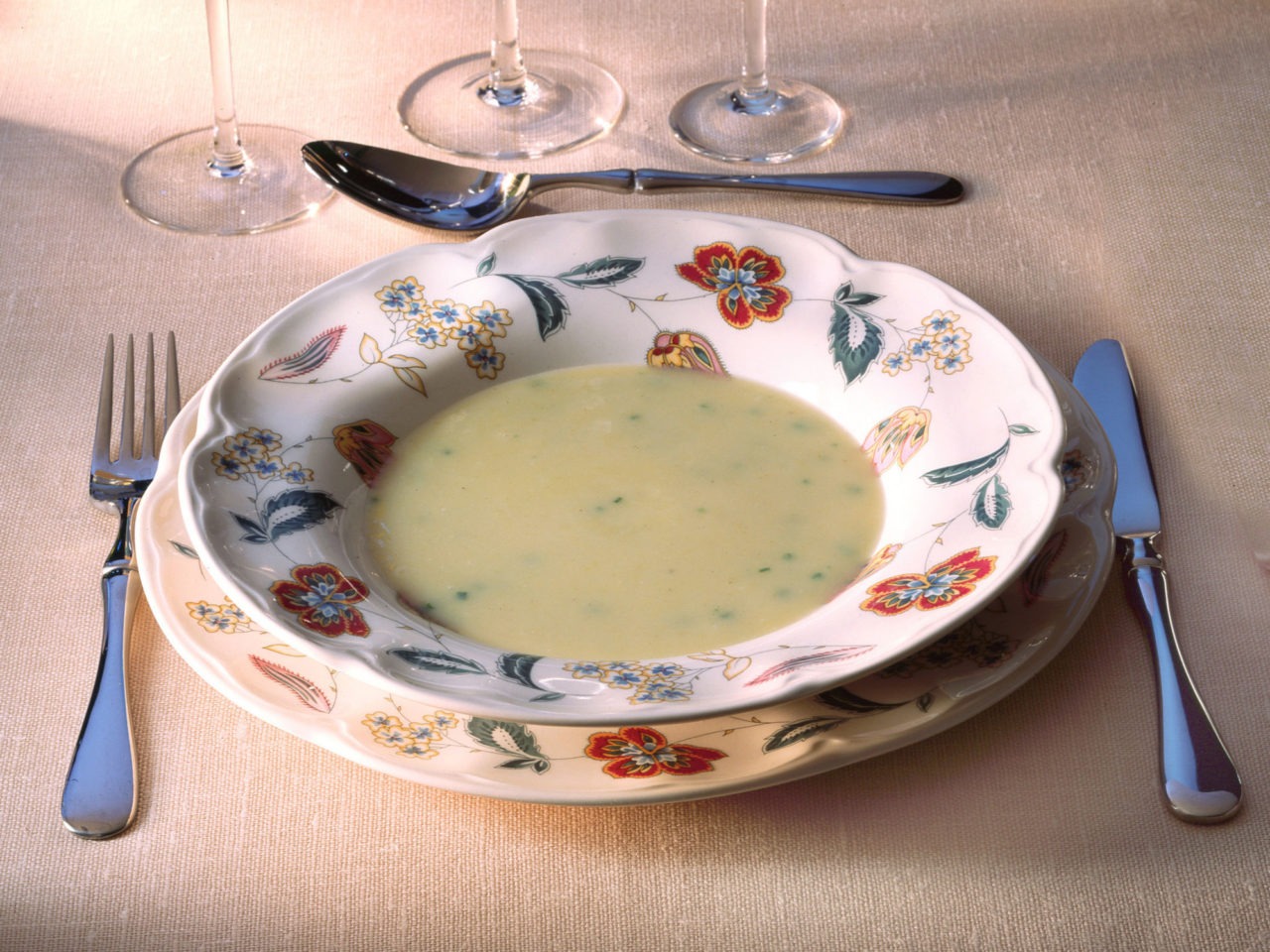 Table set for one with white floral patterned porcelain, plates and cutlery.