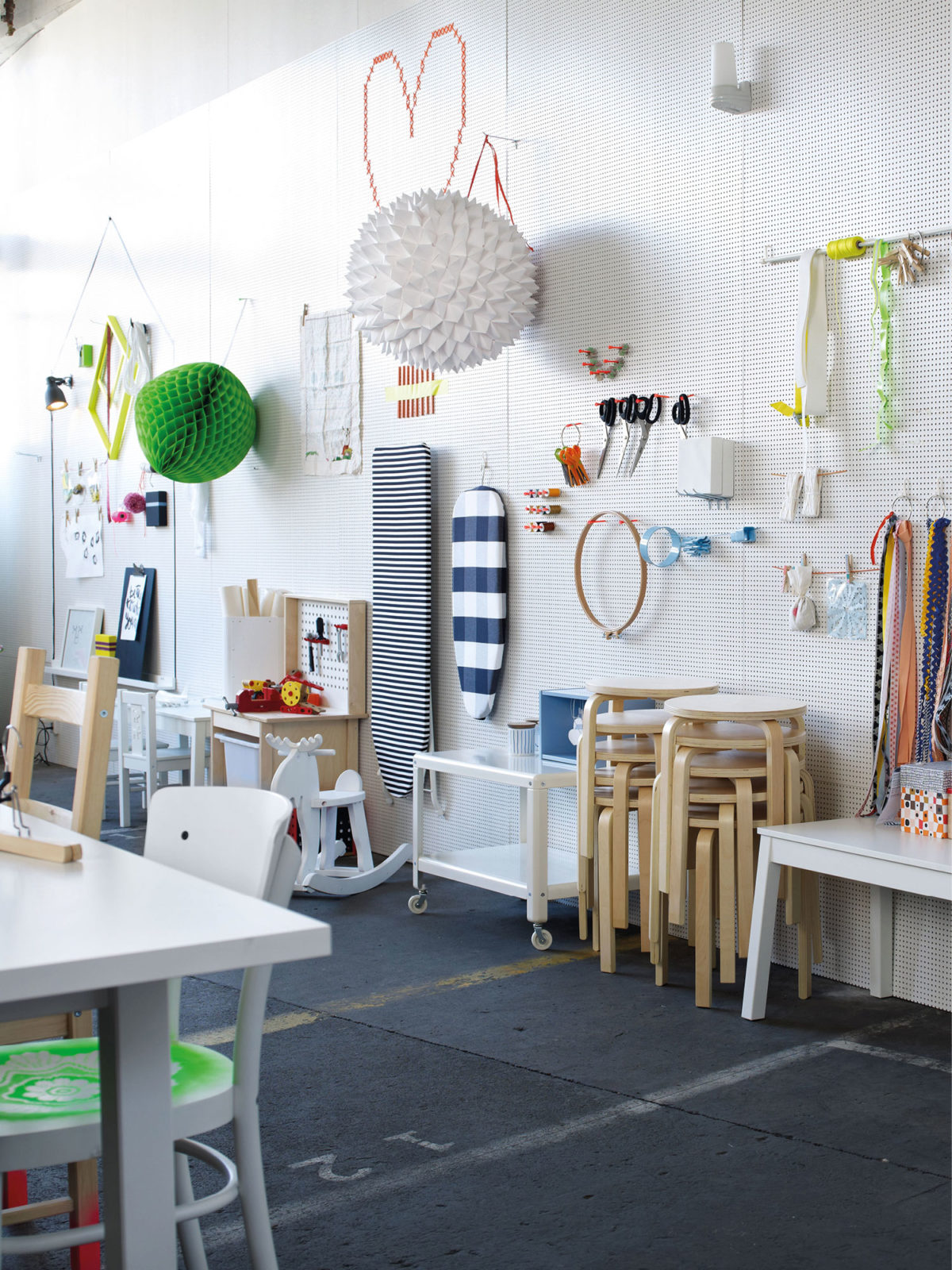 White wall holds tools, textiles, ironing boards and decorations. In front are stacked stools, tables and storage.