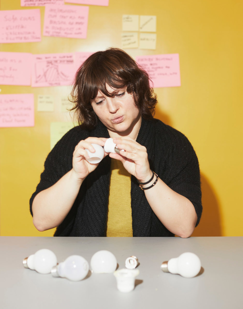 パウリーナ・パヤックが、LED電球のパーツが散らばるテーブルで2つのパーツを手に取り、じっくりと観察している。