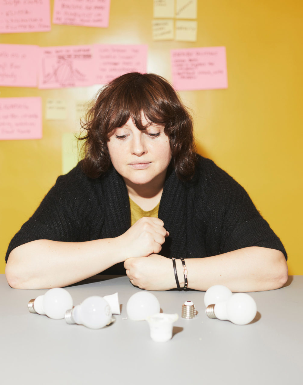 パウリーナ・パヤックが、グレーのテーブルの上に散らばったLED電球とLED電球のパーツをじっと見つめている。