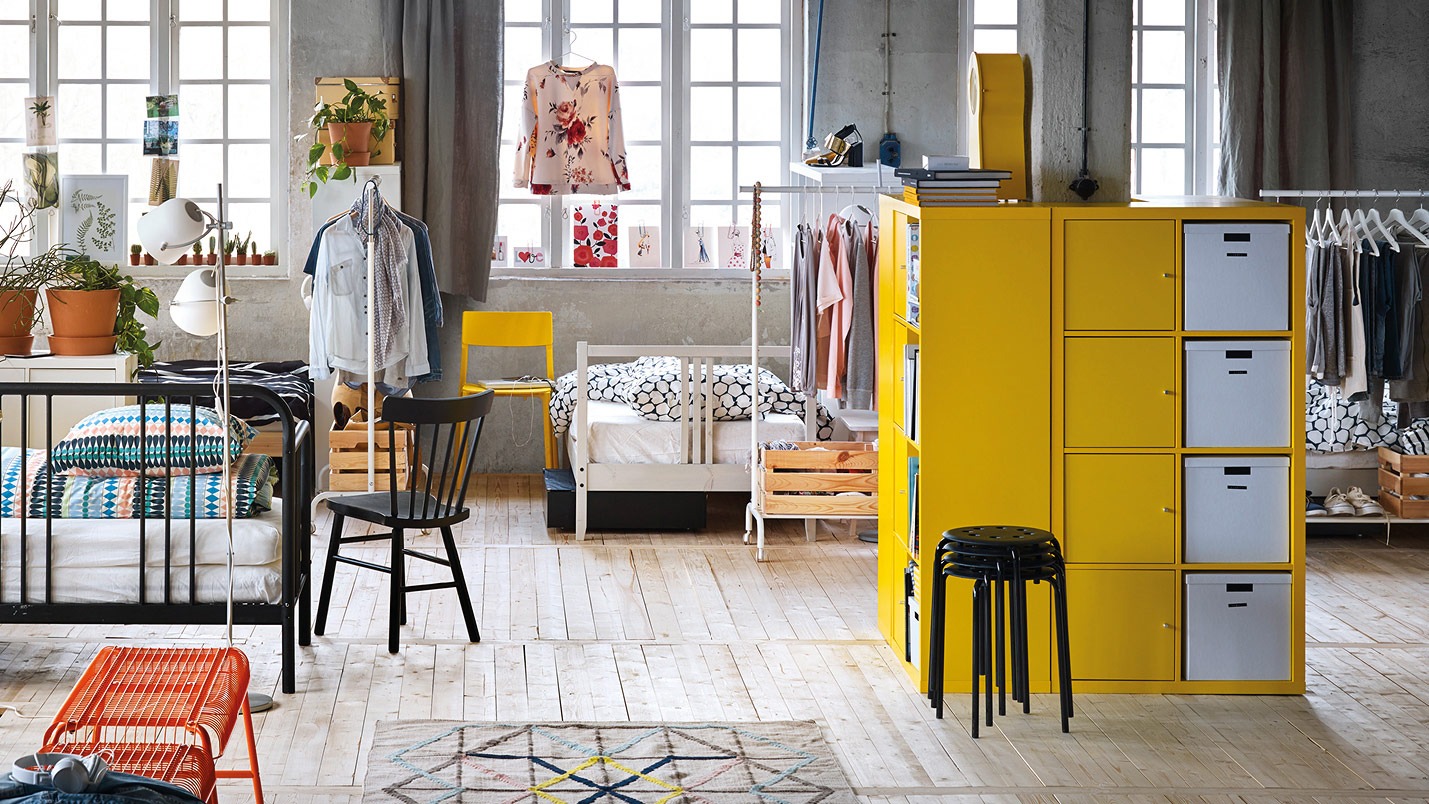 Bedden, stoelen en opbergmeubels in gedurfde maar ook rustige kleuren, als eilanden in een grote ruimte met houten vloeren.