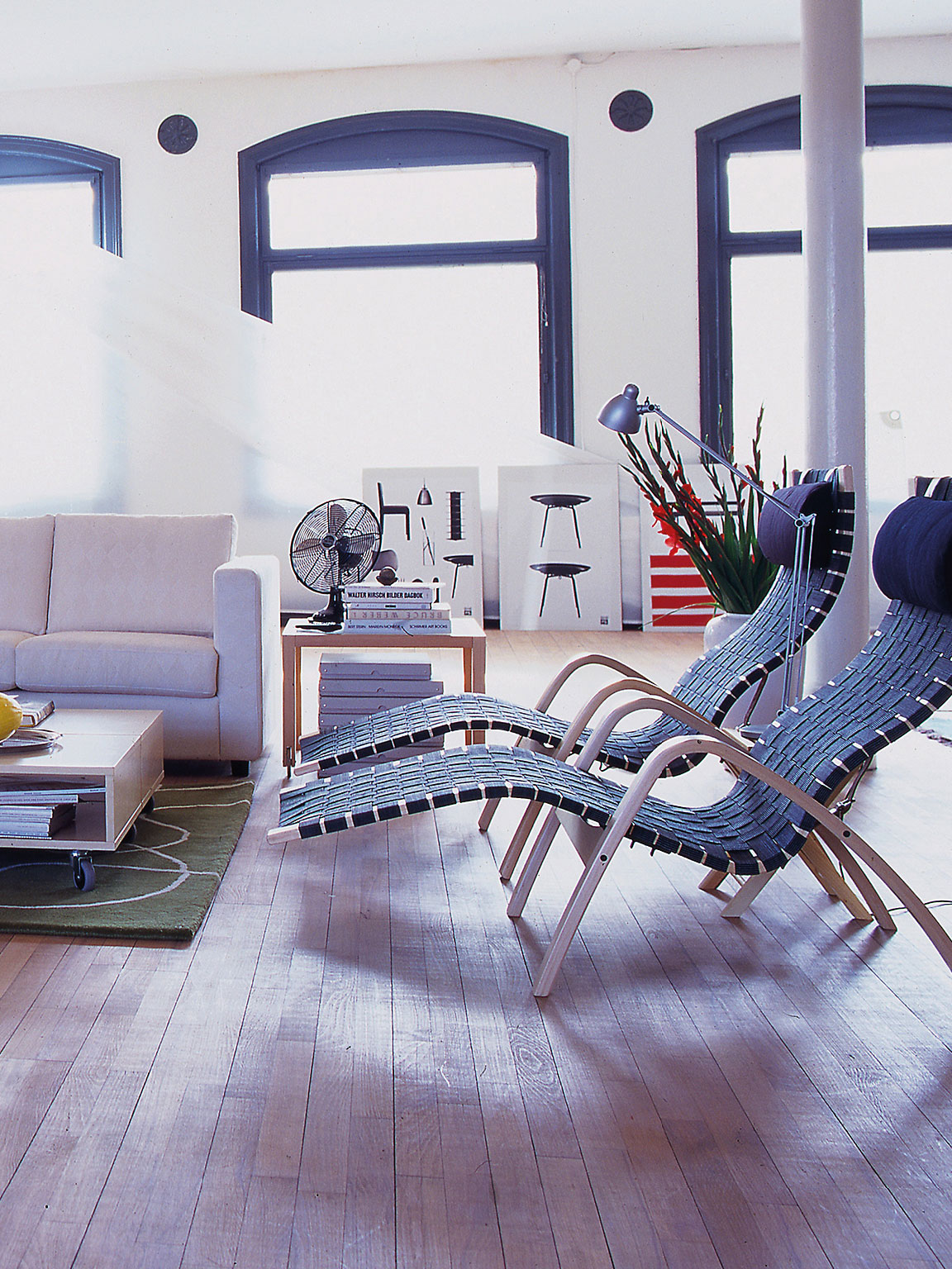 一间非常宽敞的房间，屋内设有立柱，地面铺设木质地板。一张带有脚轮的低矮咖啡桌，周围摆放着一张沙发、一把扶手椅和两把躺椅。