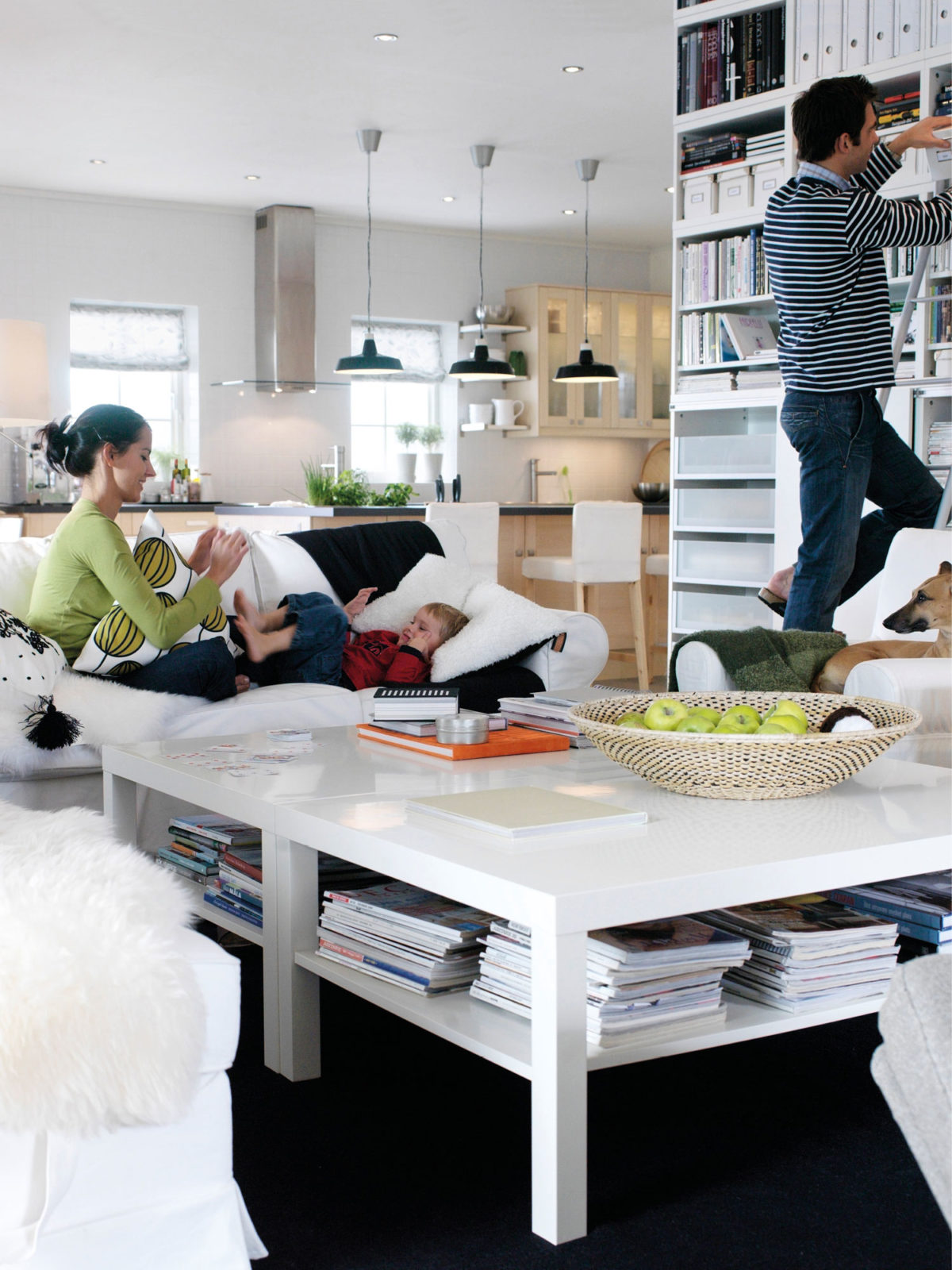 A family with children and a dog spread around a large, light family room with an open-plan solution. The furniture is either light wood or white.