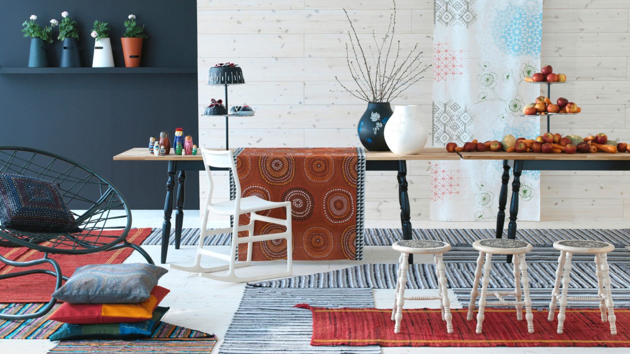 Colourful living room with large table with fruit and decorations, floor pillows, rugs and white wooden stools.