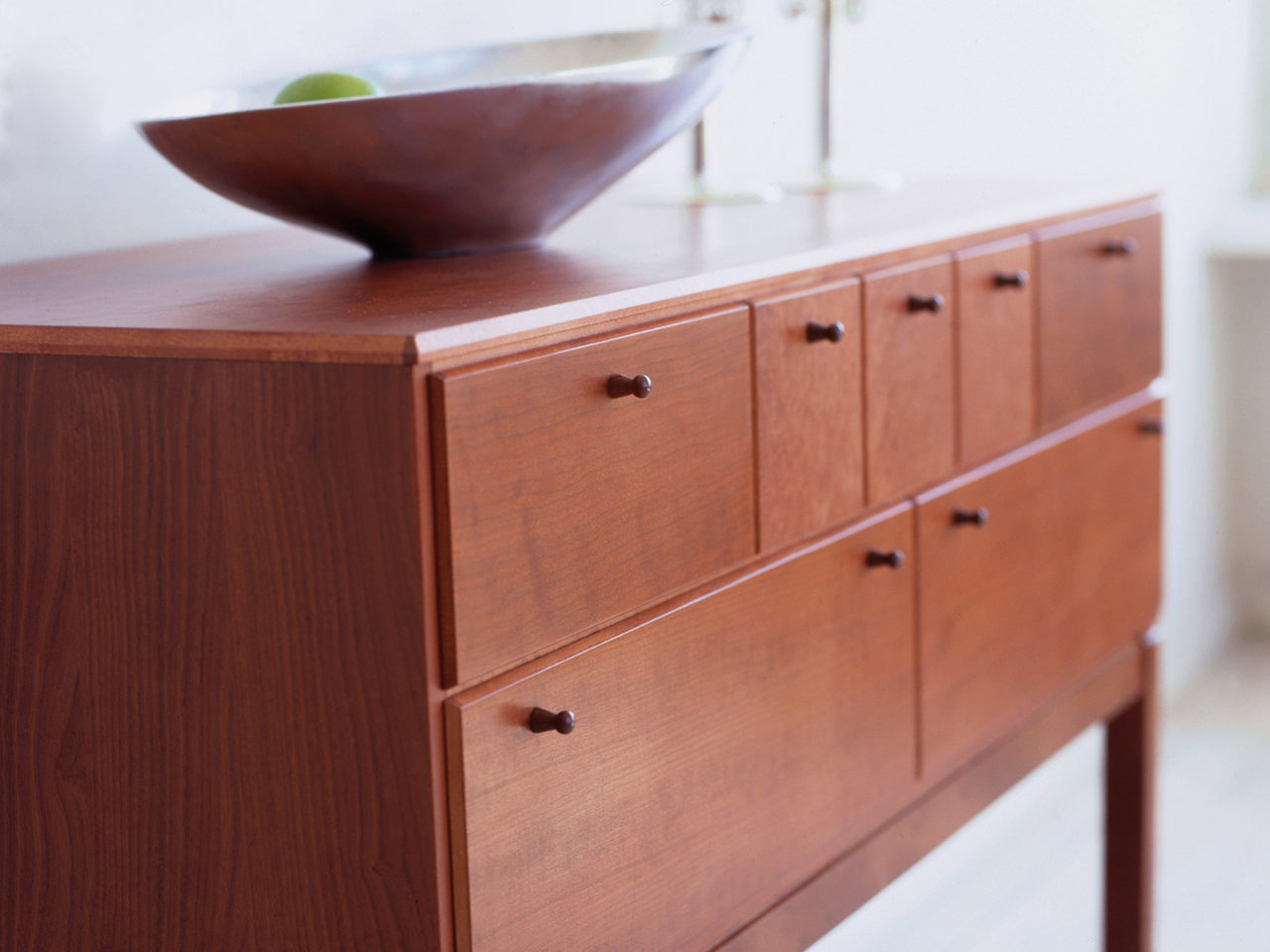 Brun låg byrå i enkel, stilren design. En fruktskål i modern form står ovanpå.