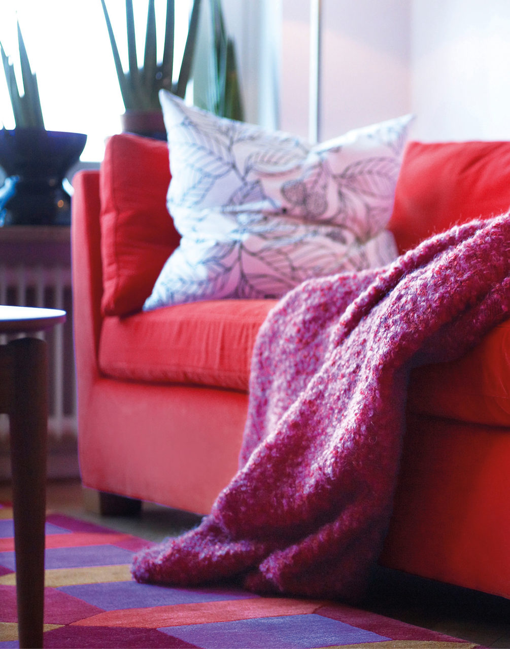 Röd soffa med vit kudde och en rödaktig filt.