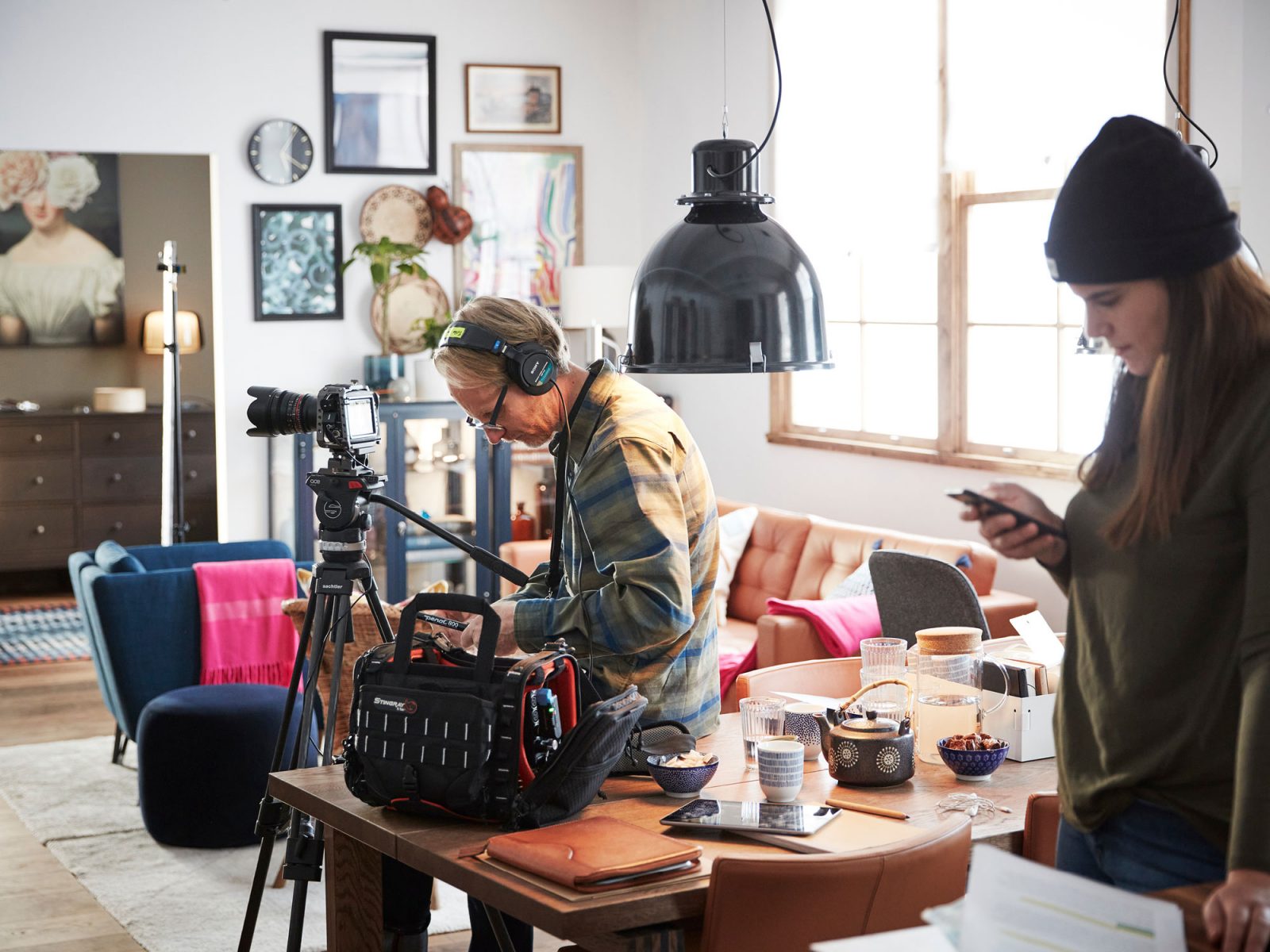 Busy production team, man and woman, stand with camera around a table in light room with modern decor.