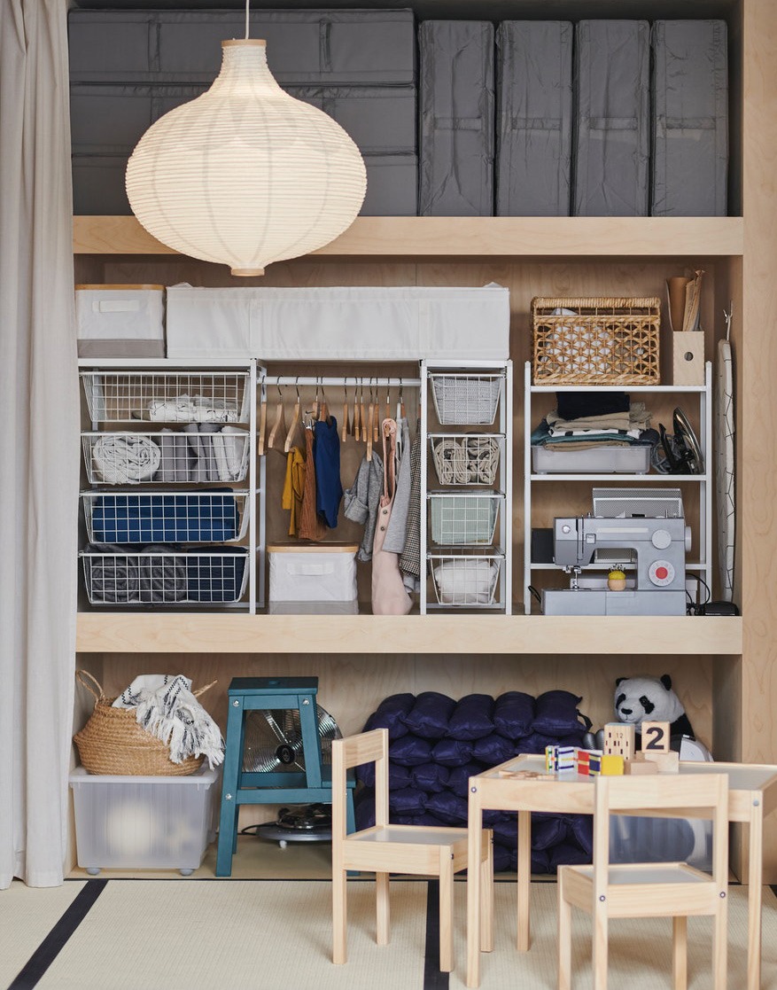 Floor to ceiling shelf with storage solutions for children’s clothing and toys. In foreground, a small table and two chairs.