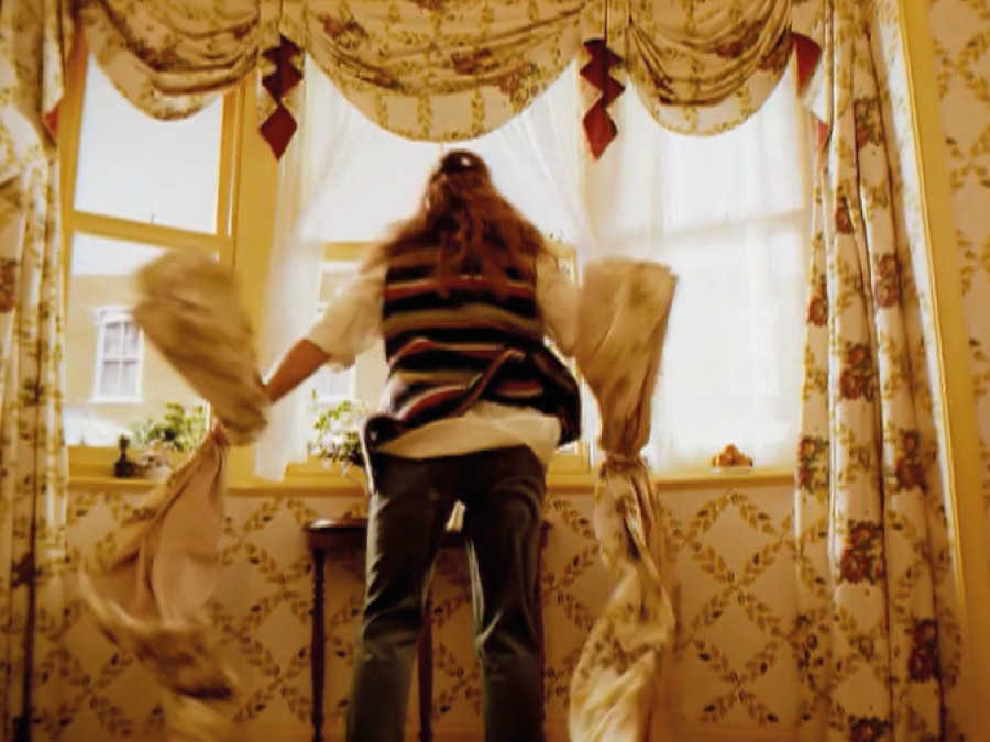 Woman seen from behind tearing down floral curtains from a large window.