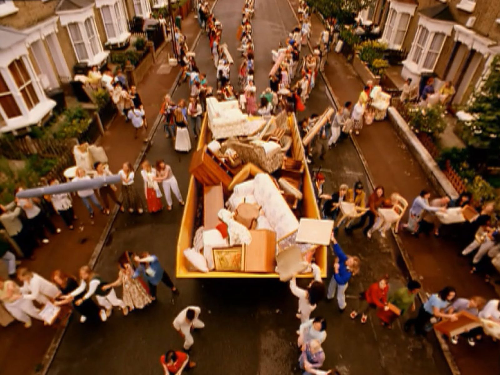 Large group of women gathered around garbage container in townhouse area, sending things from front doors to the container.