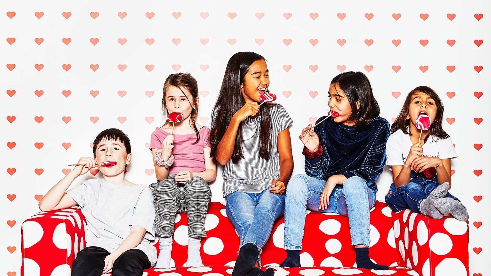 Five children of different ages relaxing in a spotty KLIPPAN sofa enjoying lollipops.
