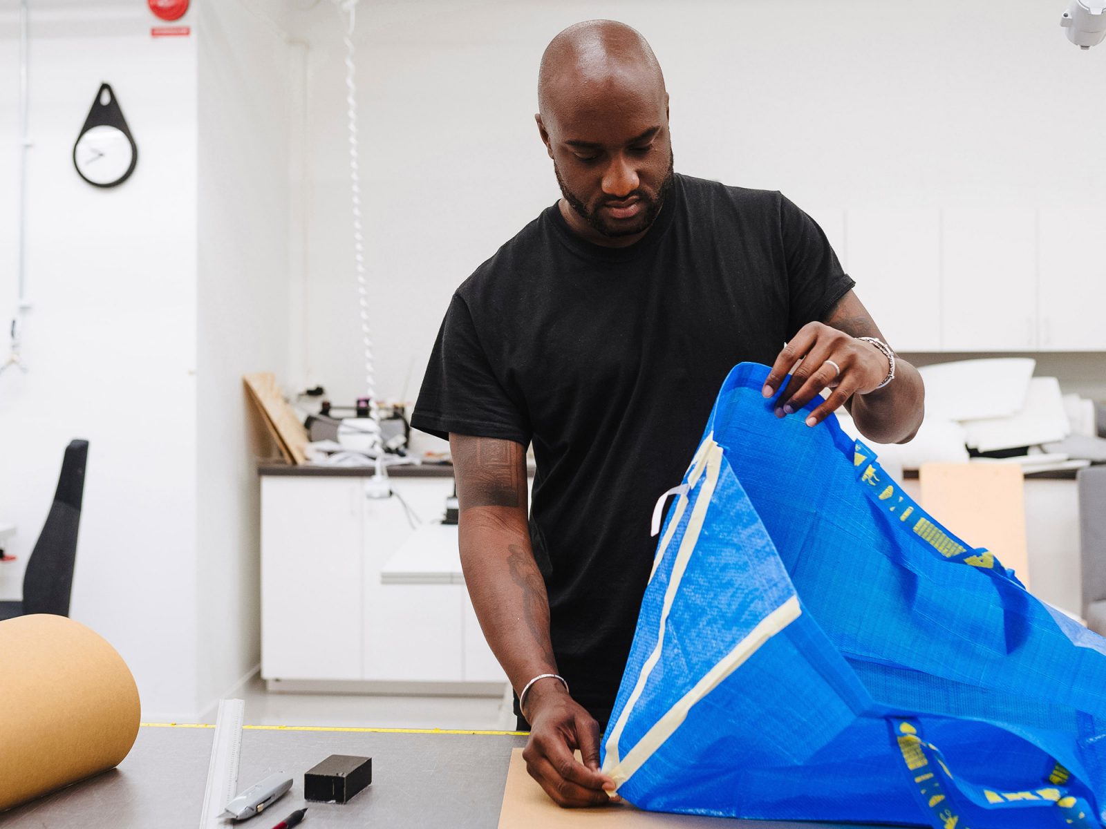 Ein Mann im T-Shirt mit rasiertem Kopf, Virgil Abloh, bei der Arbeit an einer Neugestaltung der blauen FRAKTA Tasche.
