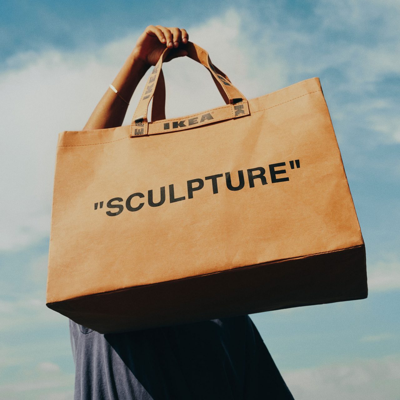 Un hombre sujeta en lo alto una bolsa marrón donde se leen las palabras «SCULPTURE» e IKEA.