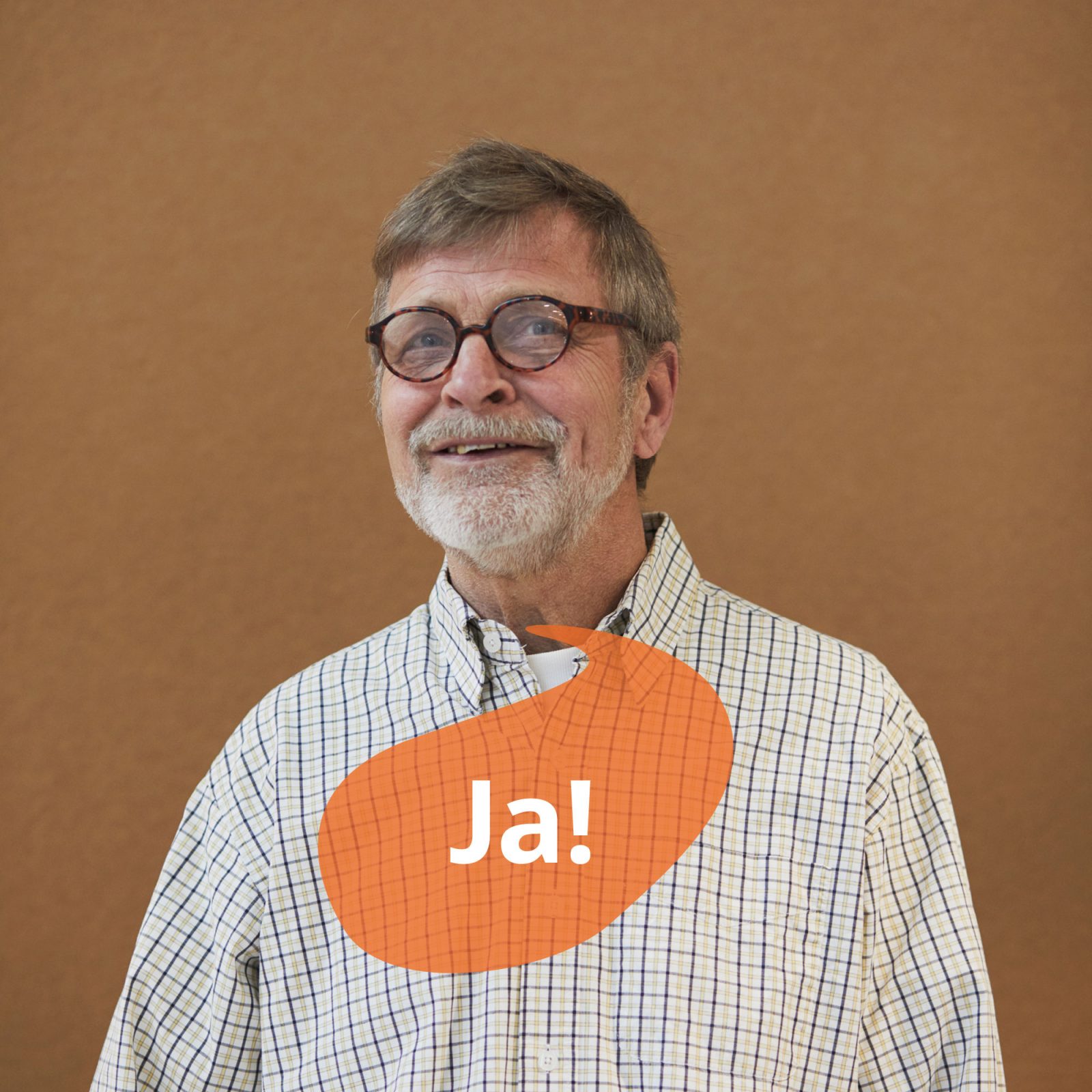 Gråhårig man i glasögon och rutig skjorta ler och tittar uppåt. En orange pratbubbla har texten 'ja'.