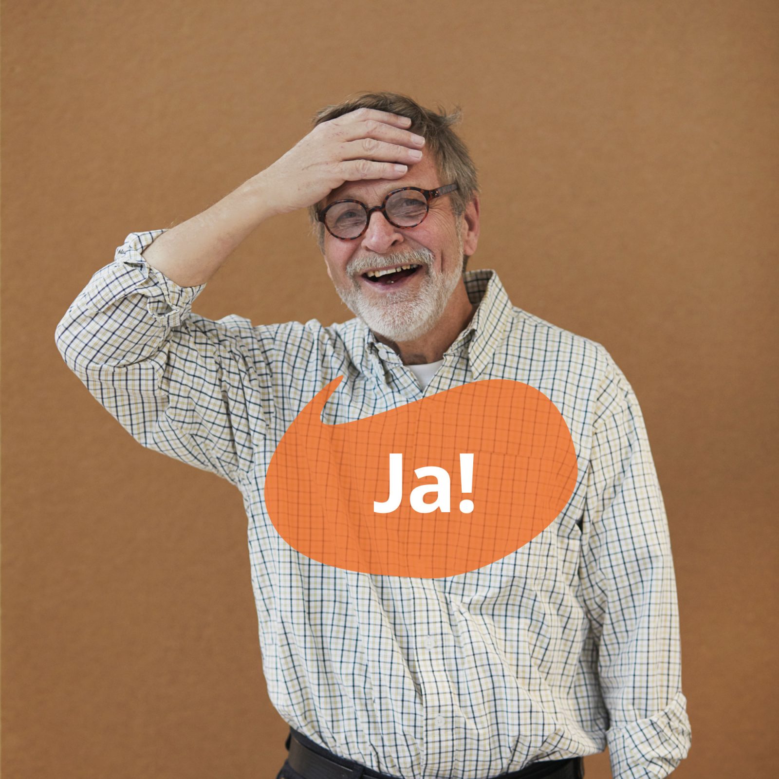 Gråhårig man i glasögon och rutig skjorta ler och håller sig för pannan. En orange pratbubbla har texten 'ja'.