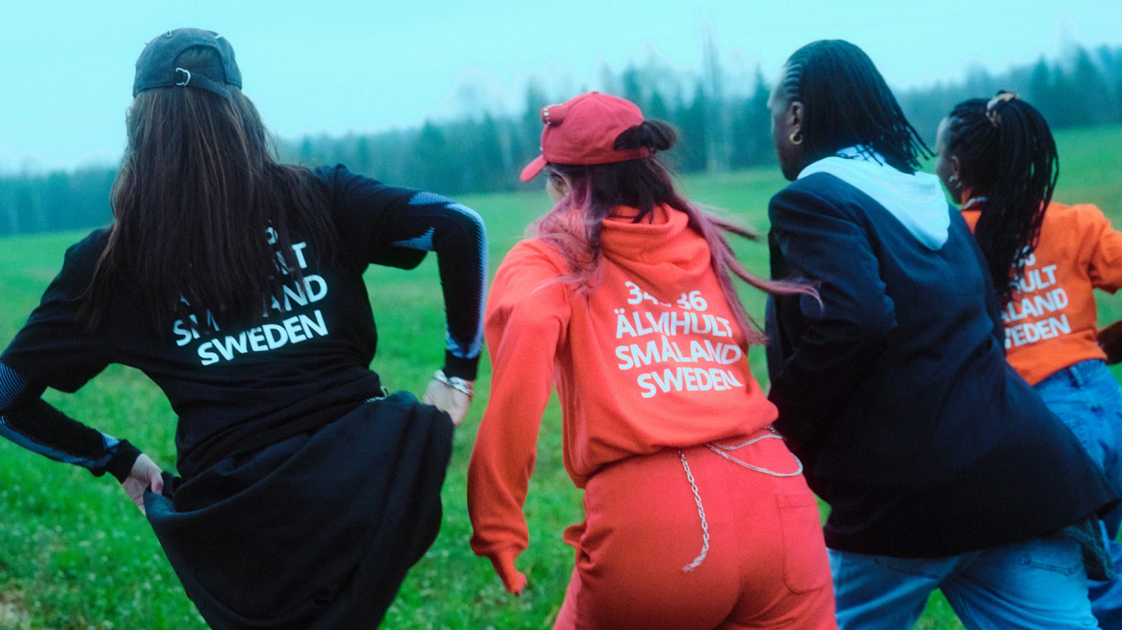 Four people running on a field, all wearing IKEA Museum new collection of cloths printed with 343 36 ÄLMHULT SMÅLAND SWEDEN.