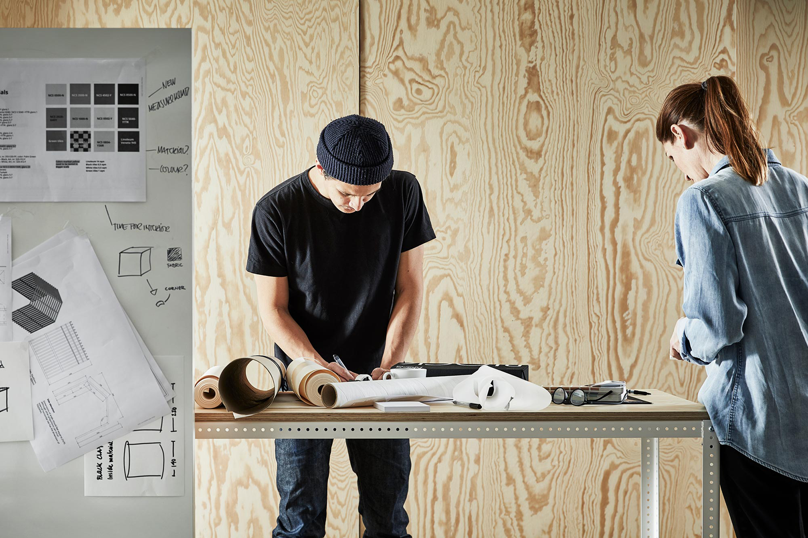 Sketches of construction and design hanging on boards and two people are working on new sketches around the table.