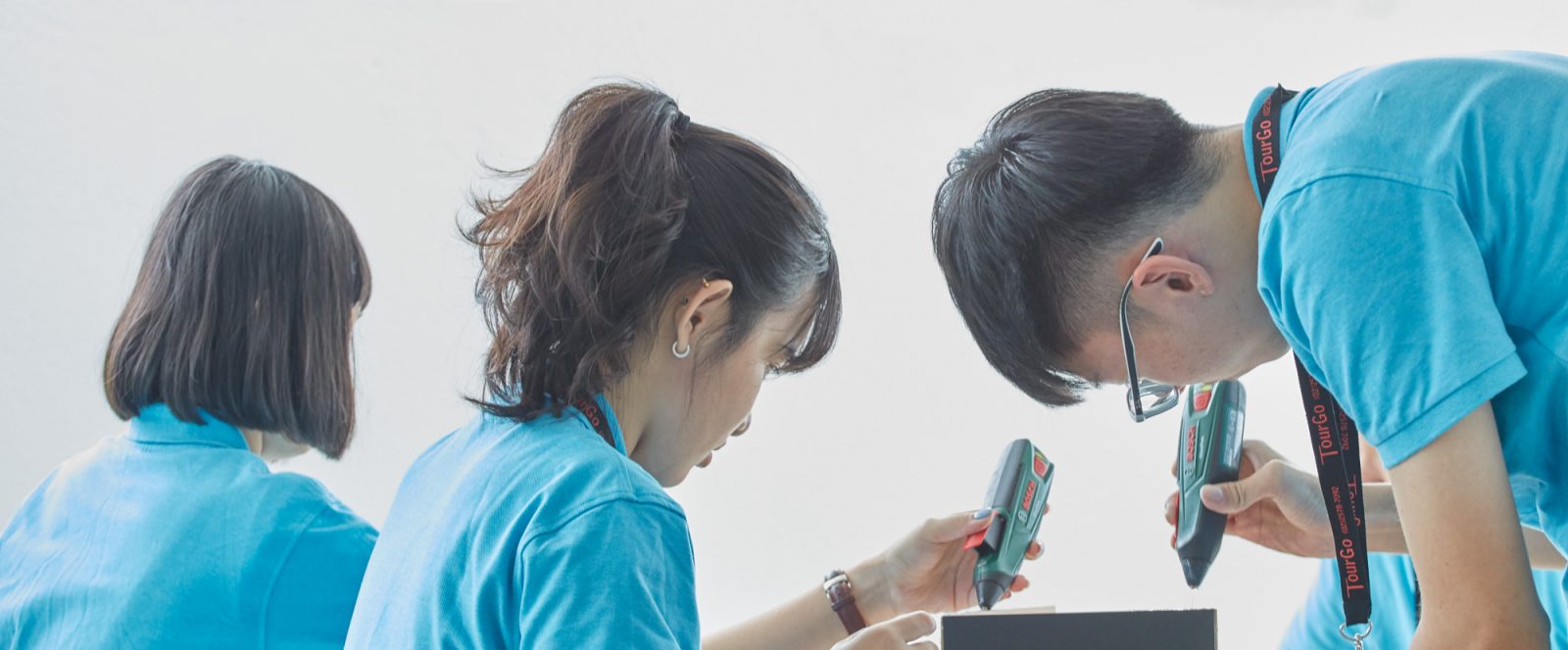 Three people in blue t-shirts doing experiment with glue guns.