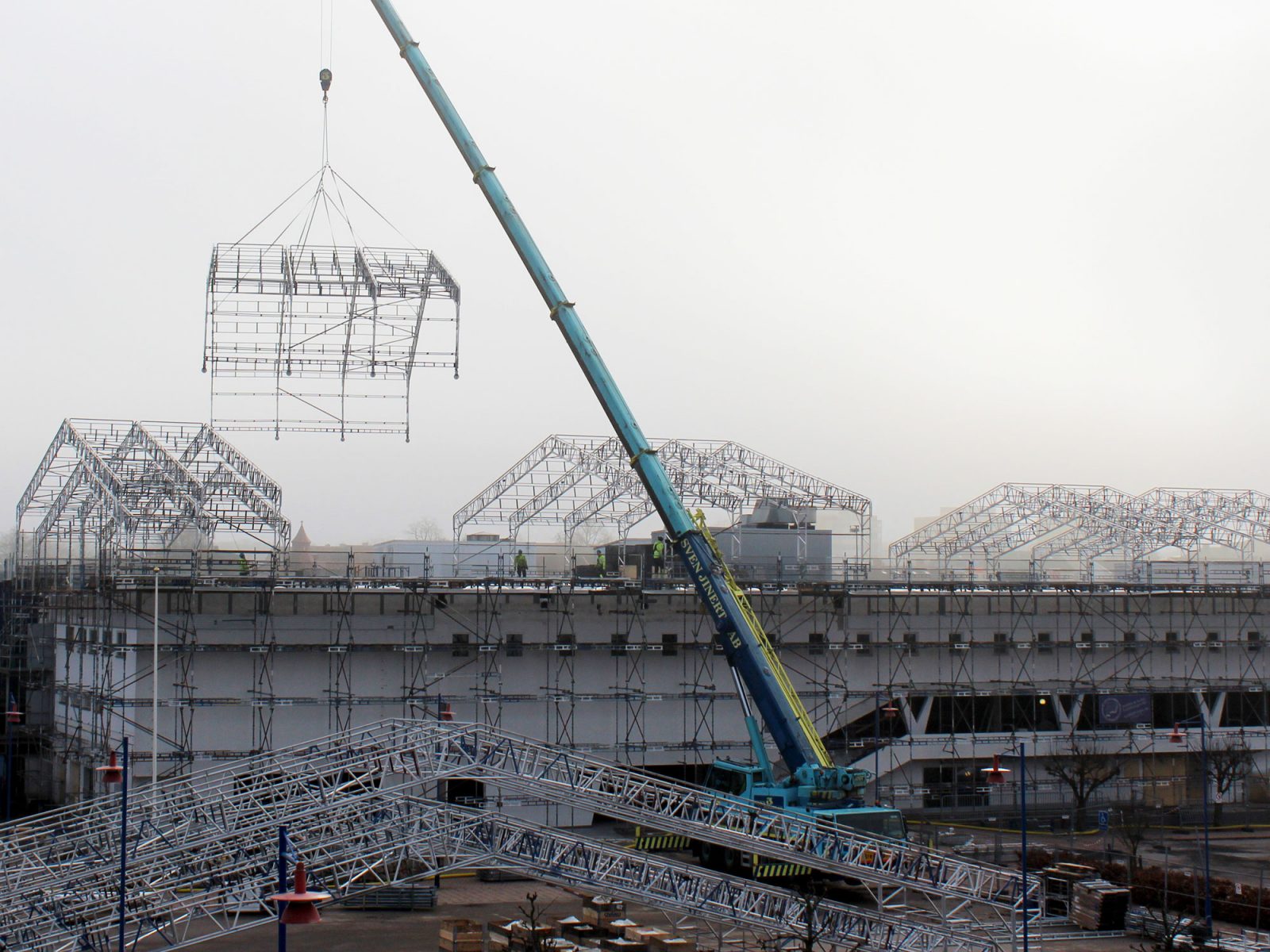 Blick auf eine riesige Baustelle. Ein großer Kran hebt Gerüstteile über ein Dach.