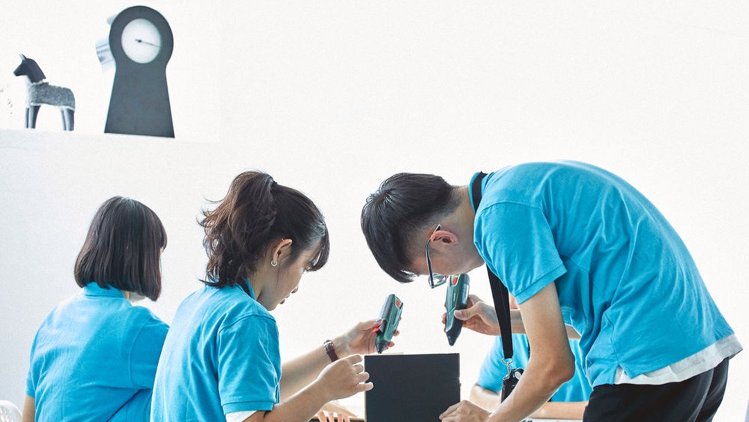 Youths in blue t-shirts gluing in a black cardboard box.