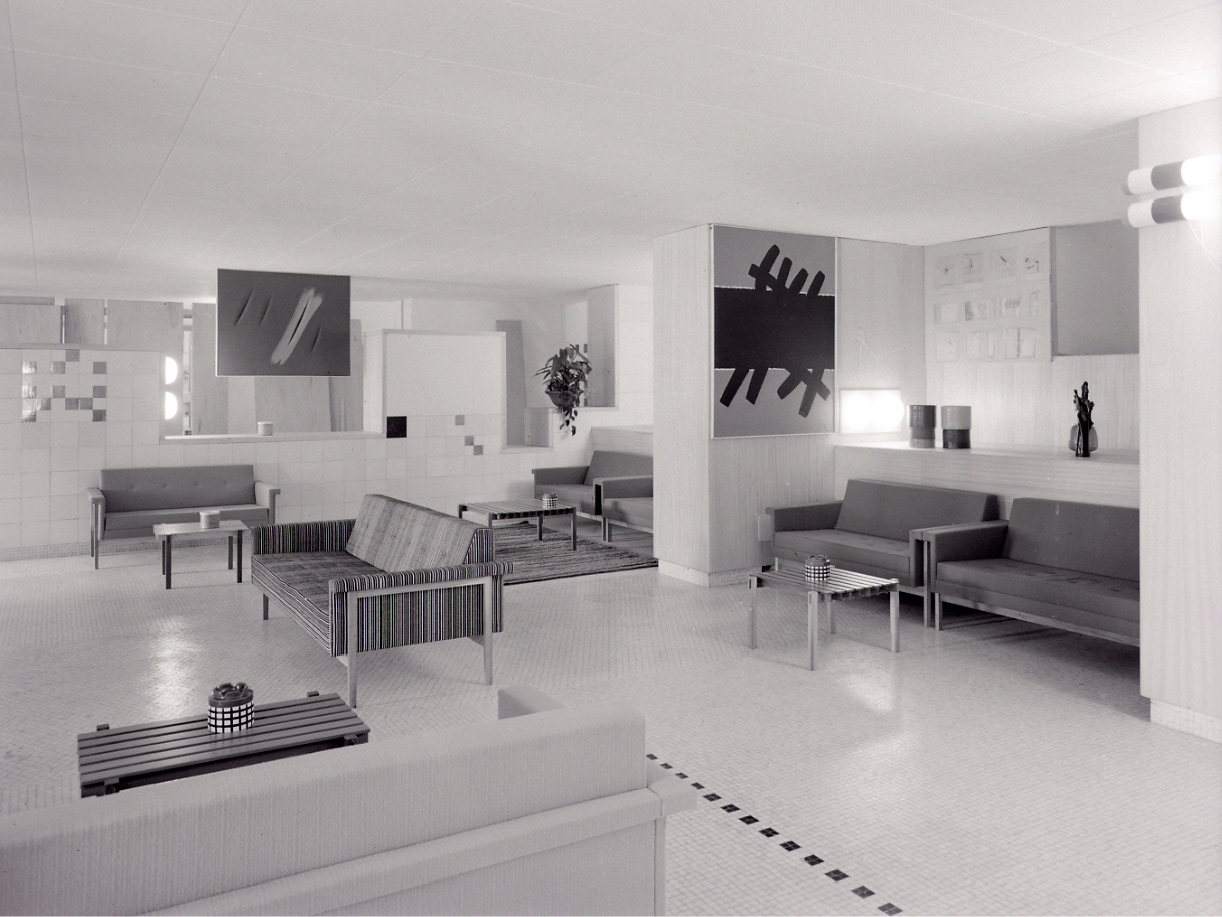 Furniture exhibition with several seating groups, stylish sofas in 1960s style with modern abstract art on the walls.