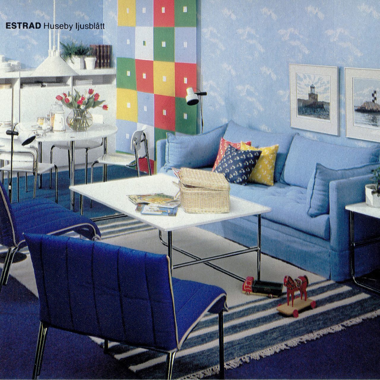 Vardagsrum i blåvita toner, himmelsmönstrad tapet och randig matta under vitt soffbord, blå fåtöljer och soffa.