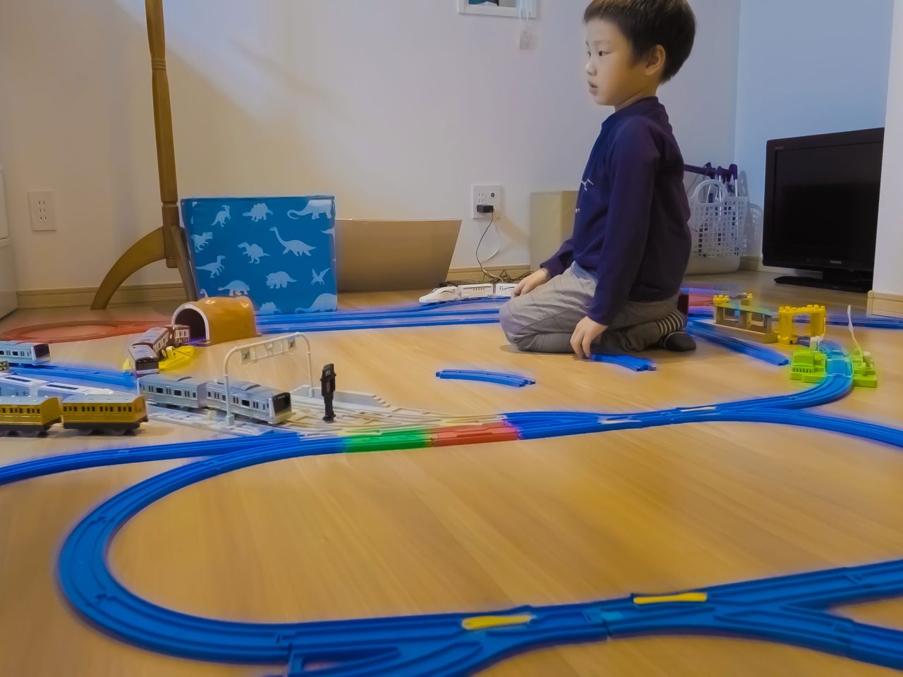 フロアデッキの床に座り、大きな線路のおもちゃで遊んでいる小さな子ども。