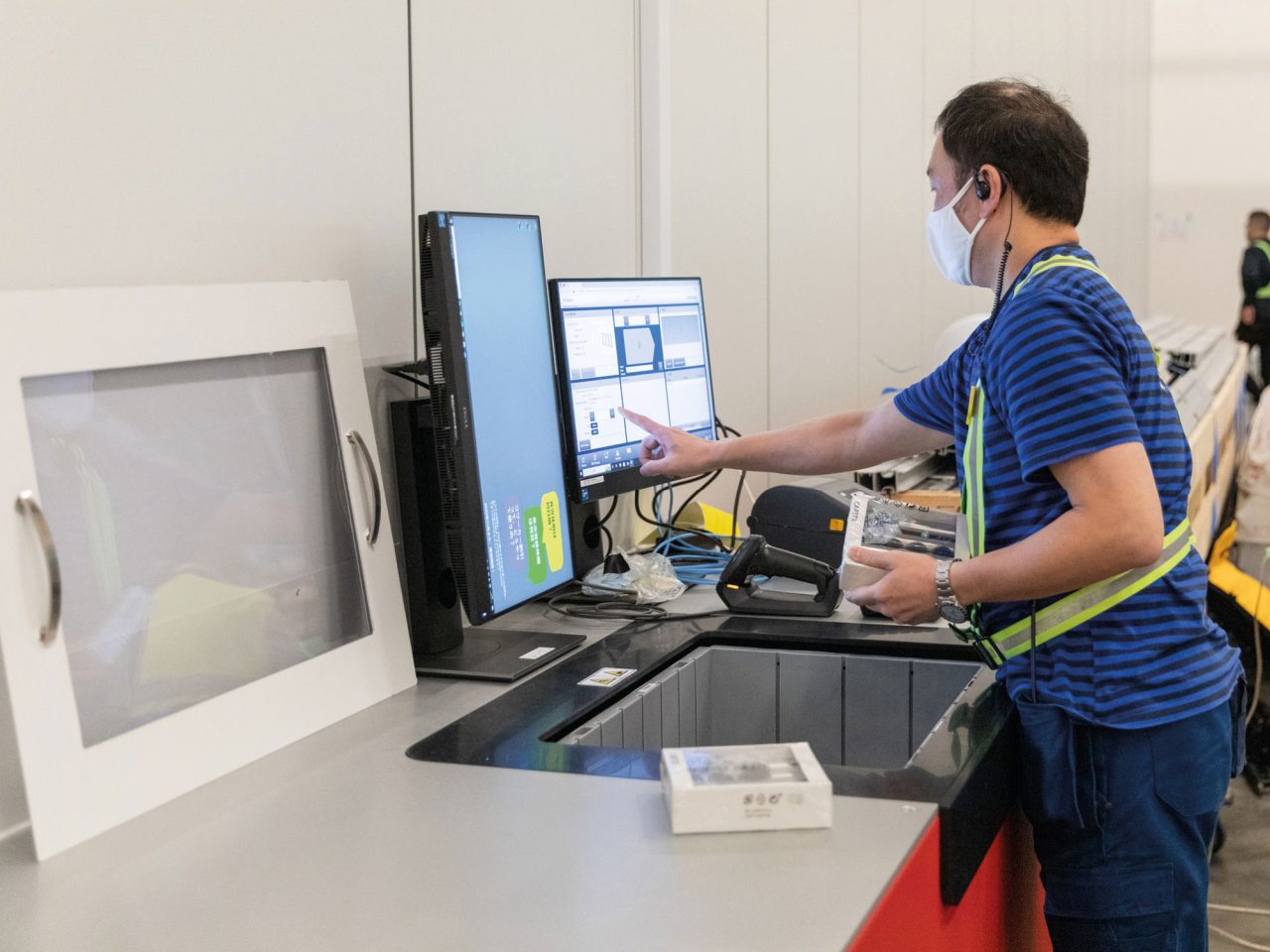 黒髪のイケアのコワーカーが、自動化されたシステムでボックスの配送をチェックし、コンピューターのスクリーンを確認している。