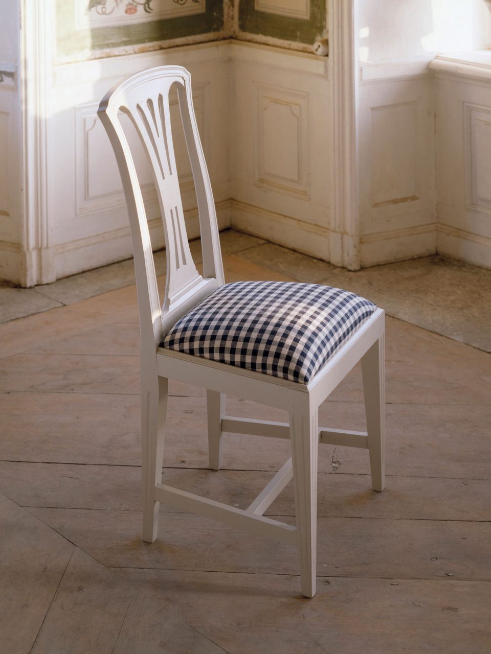 Simple white chair in Gustavian style with upholstered seat covered in blue and white check fabric.