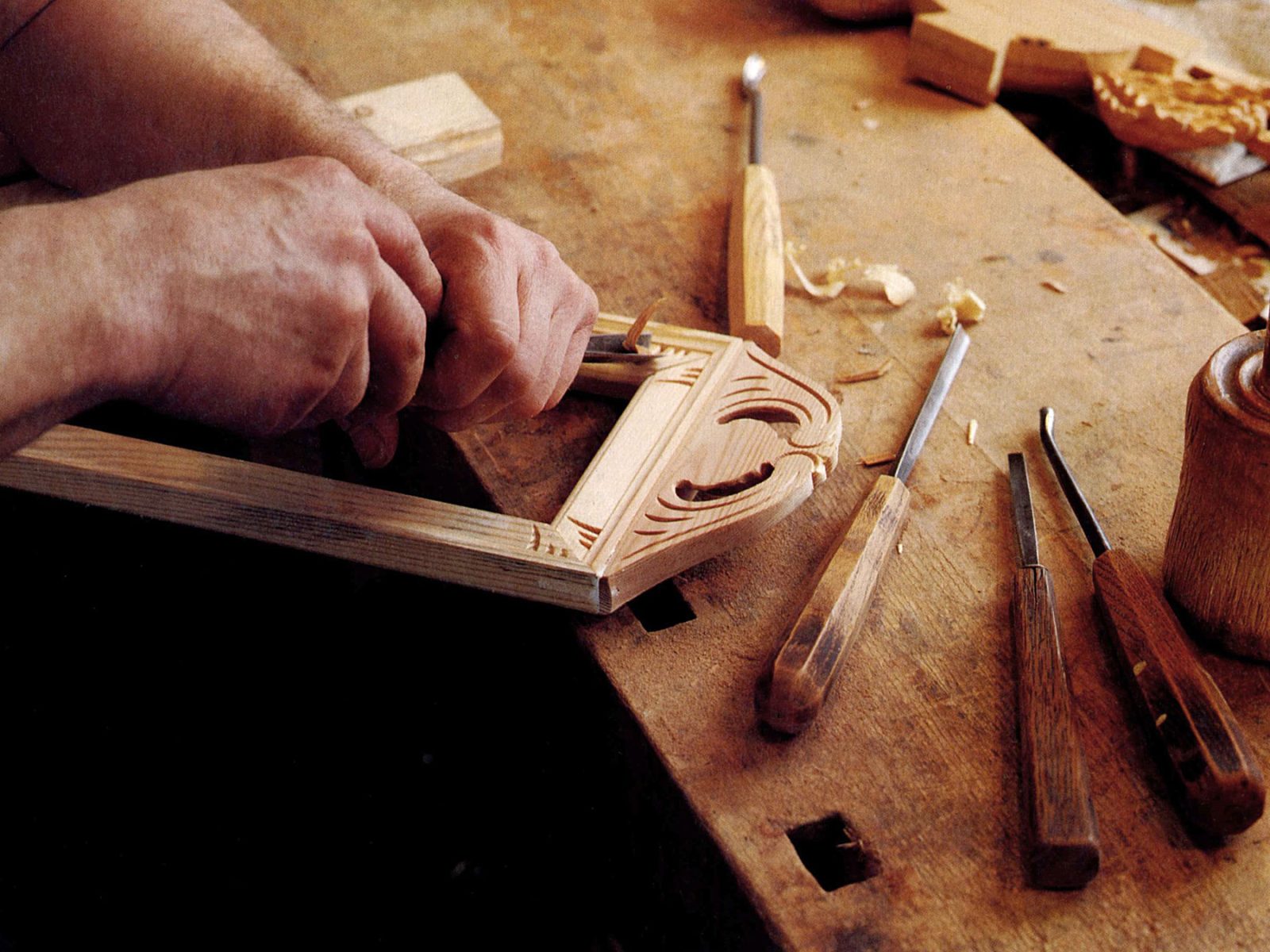 Close-up of a person carving a wooden frame at a rustic carpenter's bench.
