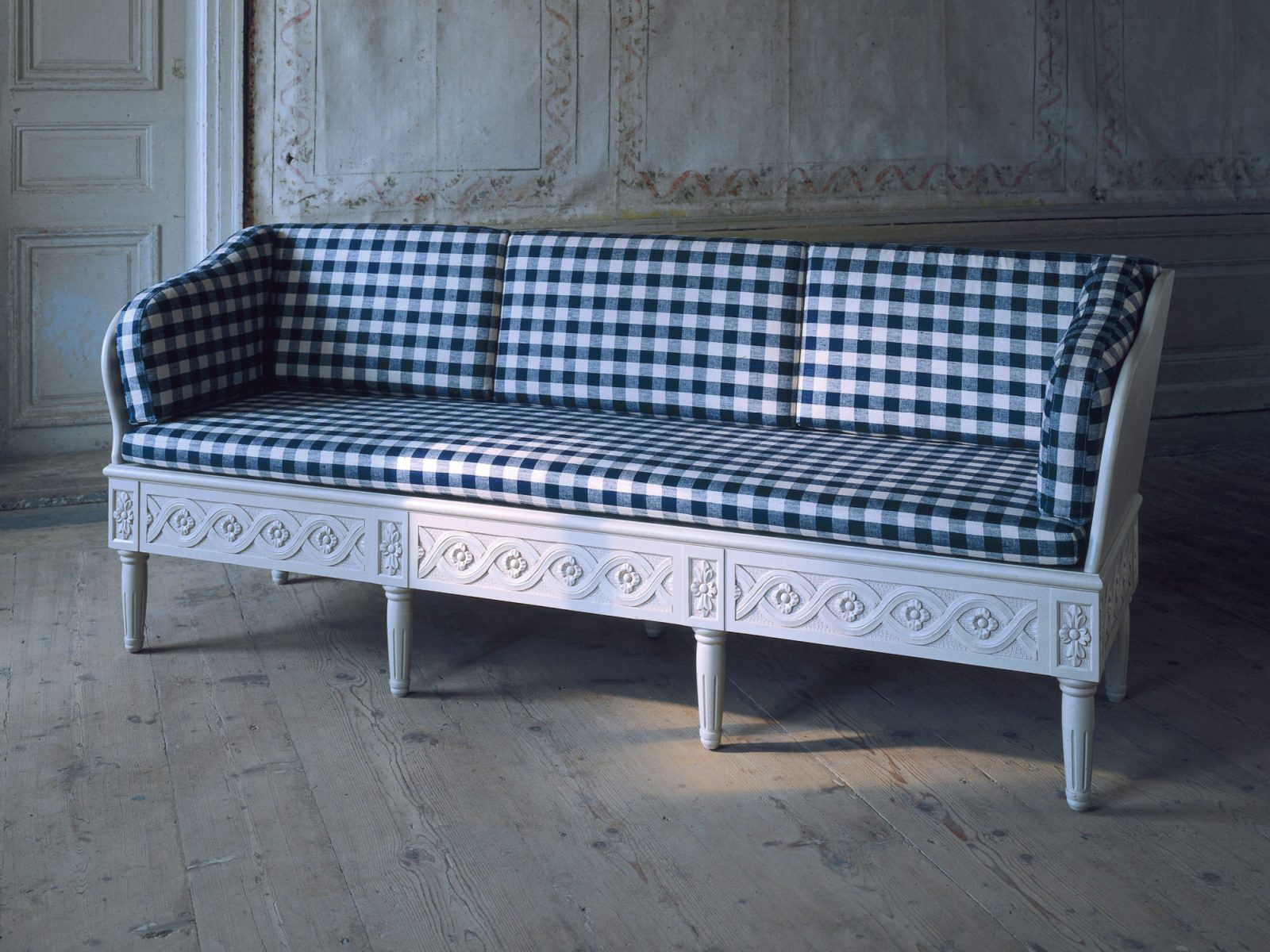 Trough sofa in light grey with blue and white check seat cushion and pillows and carved strapwork on the frame.