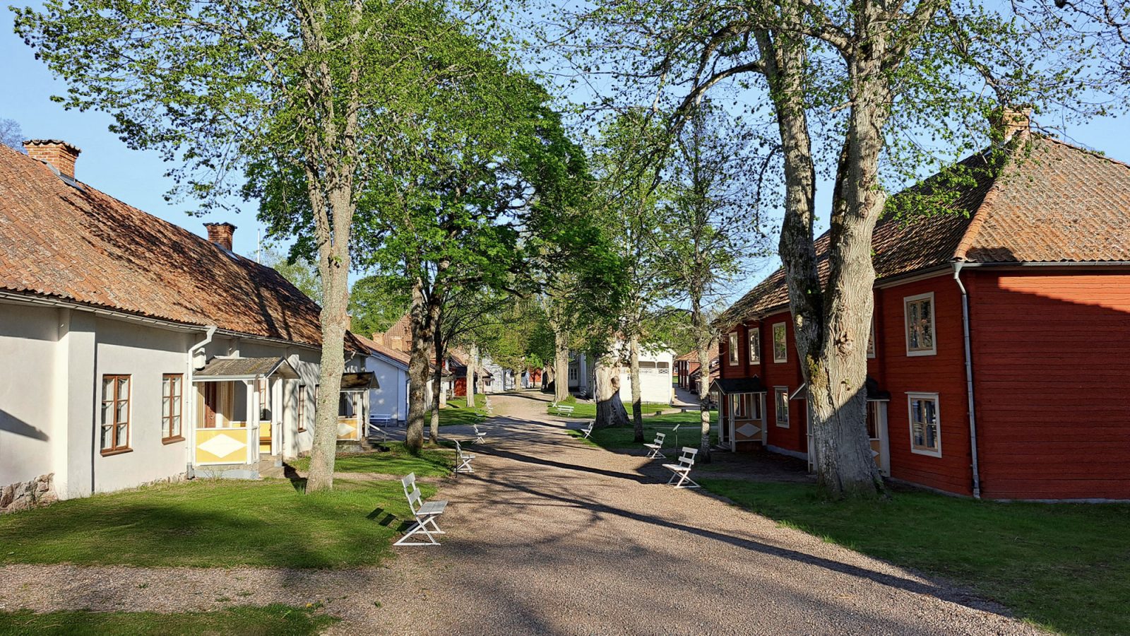 Gravel road lined with older buildings and lush trees, Medevi spa, Sweden.