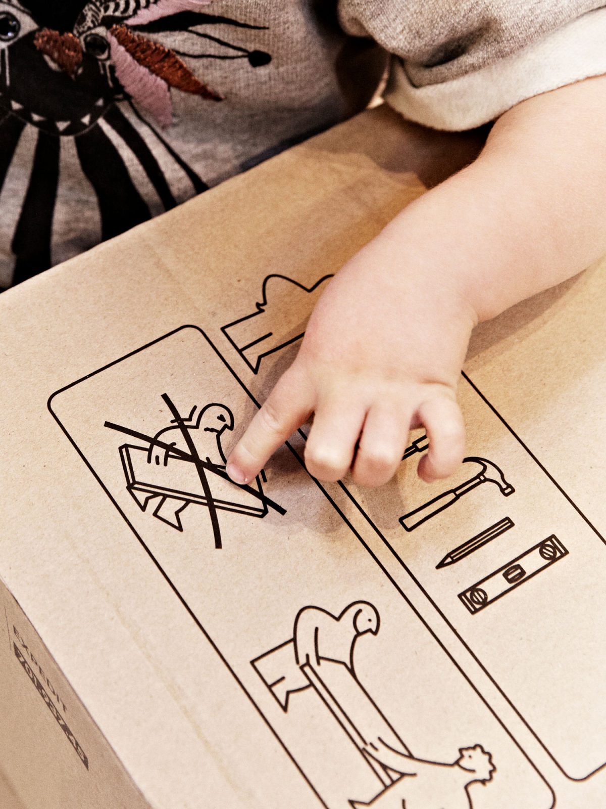 A small child's hand points at a drawing on an IKEA flatpack, showing how the package should be carried.