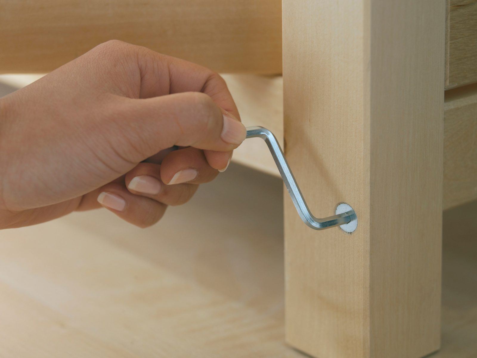 Close-up of a hand using an Allen key to screw a screw into light wood.
