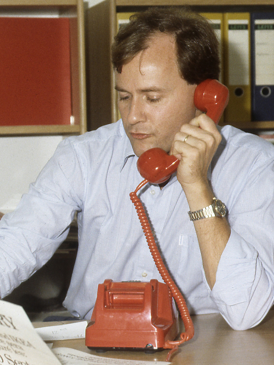 Man in light blue shirt, Jan Kjellman, talking on a red phone.
